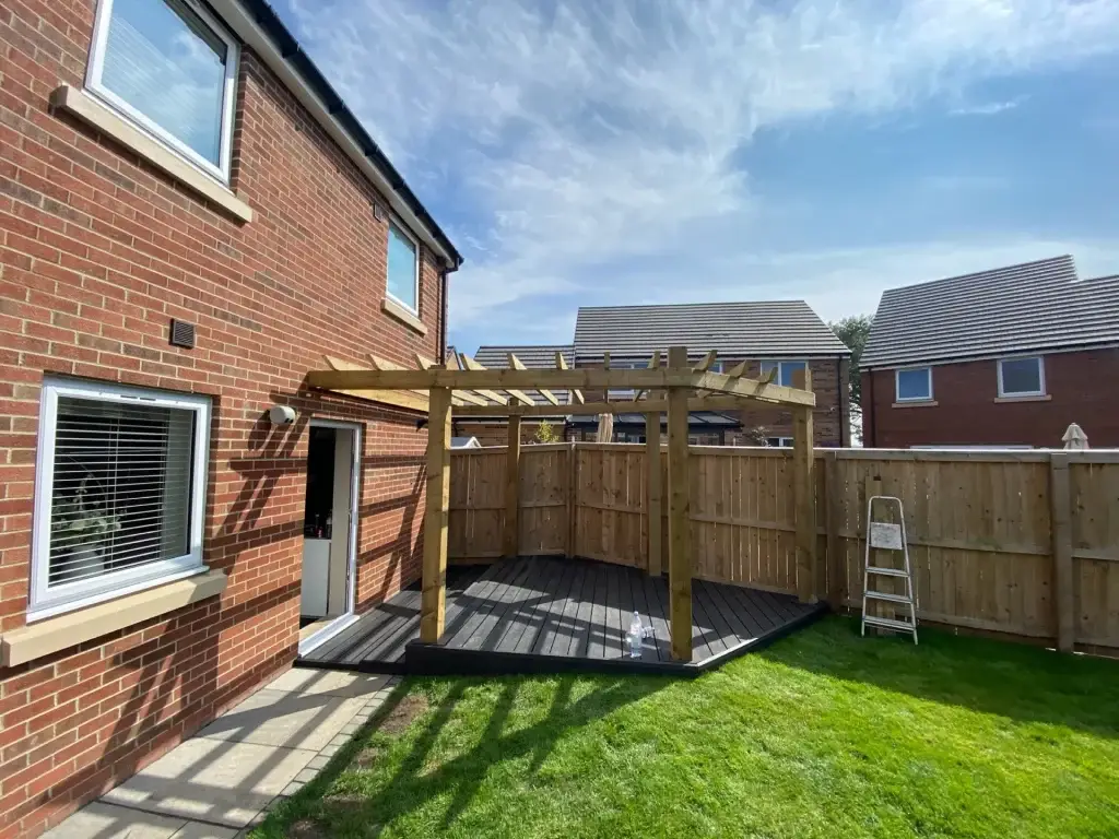 A chunky timber pergola over black composite decking behind a new-build house