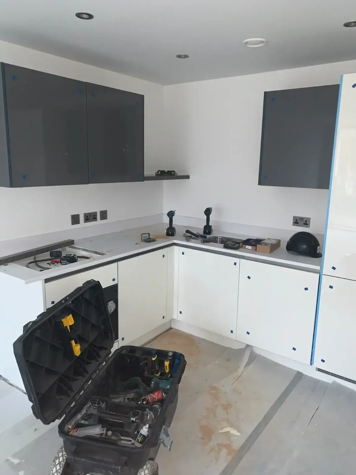 A white kitchen with grey wall units, part way through fitting