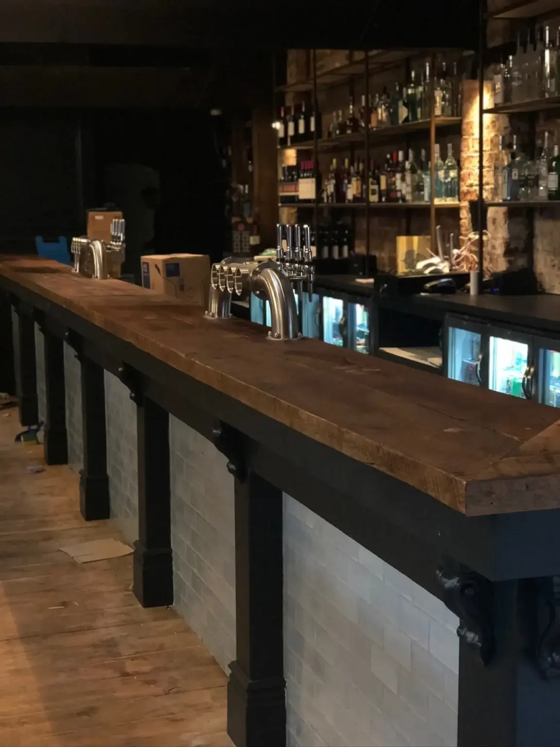 A long hand made bar counter with a rustic timber top on black posts