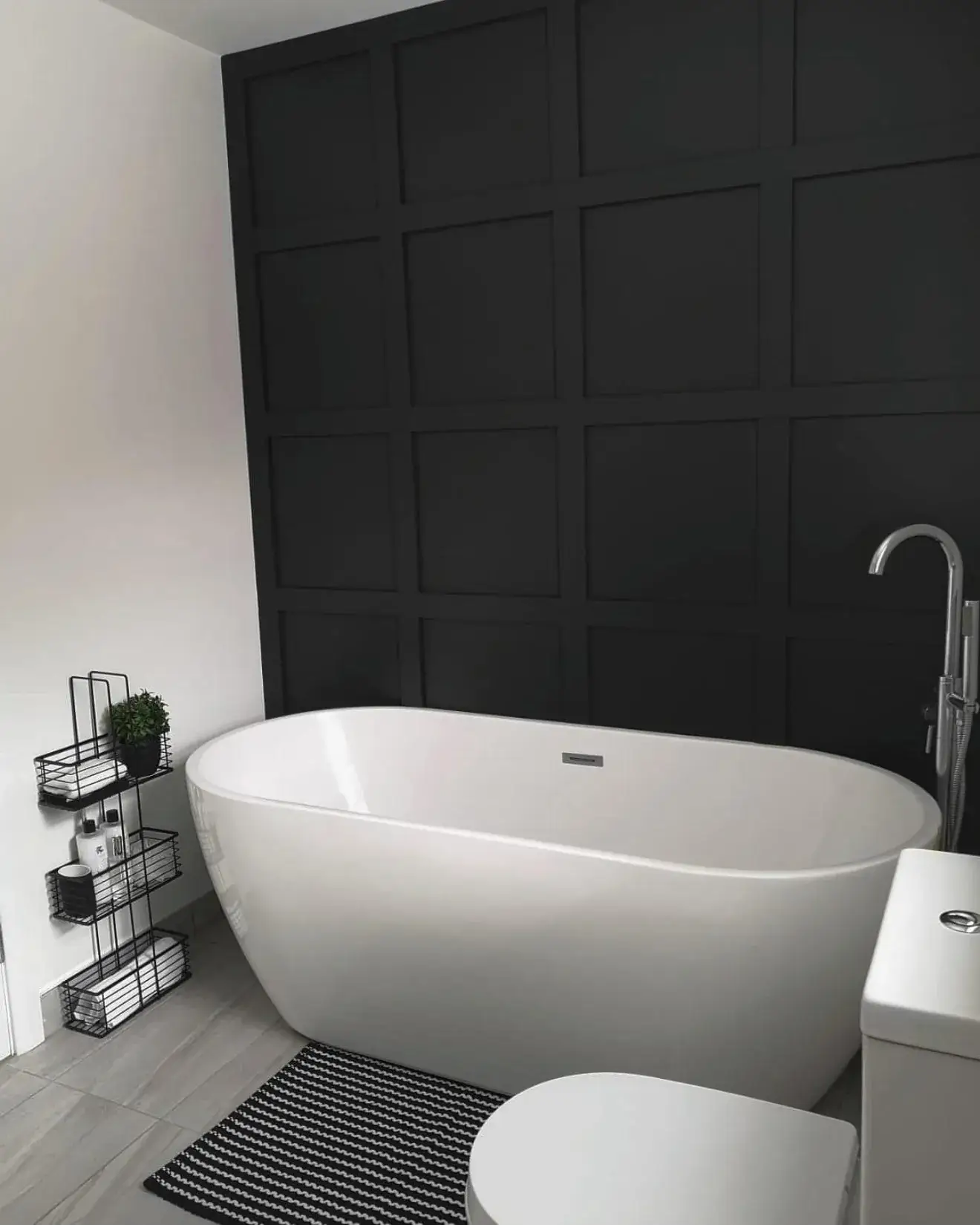 A freestanding bath in front of a dark panelled wall