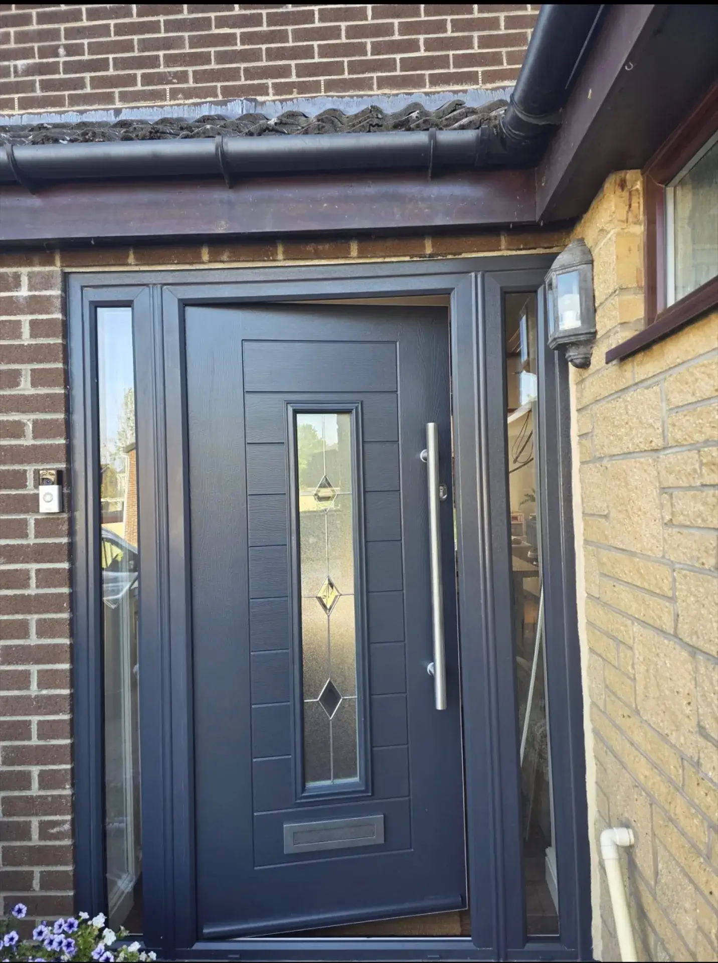 A grey composite front door with a glazed panel and side light