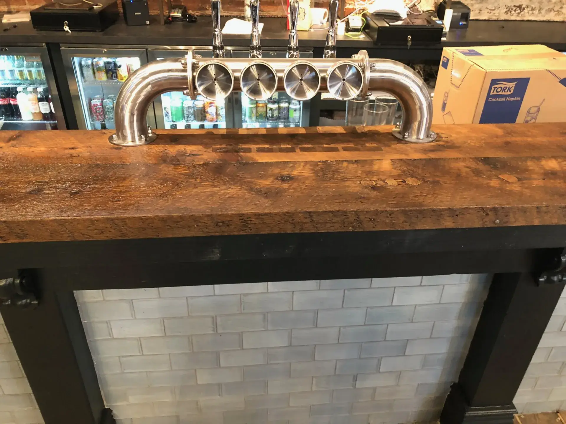 A rustic timber bar top with beer taps, over a tiled front