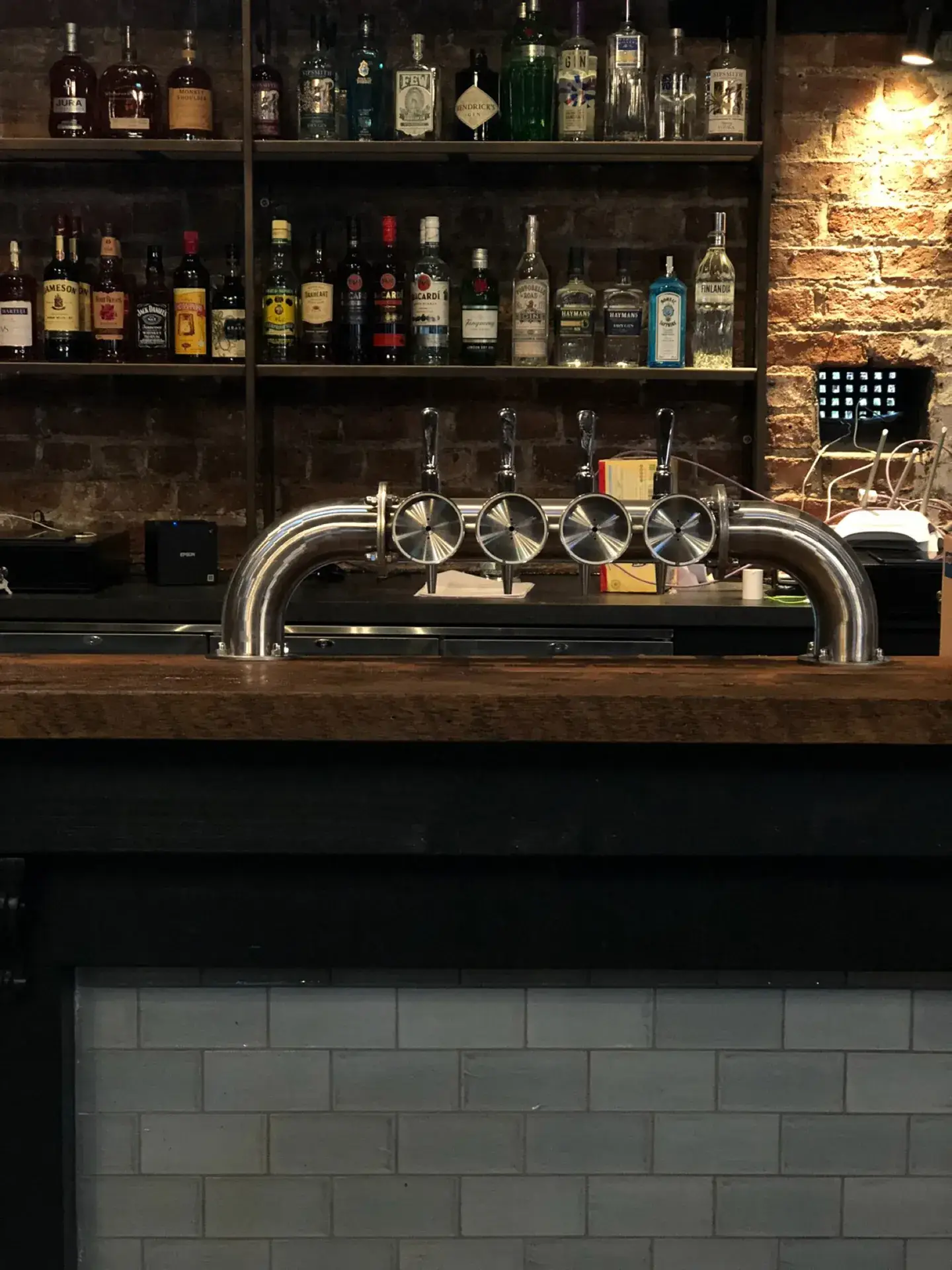 A timber back bar with shelving and taps against exposed brick