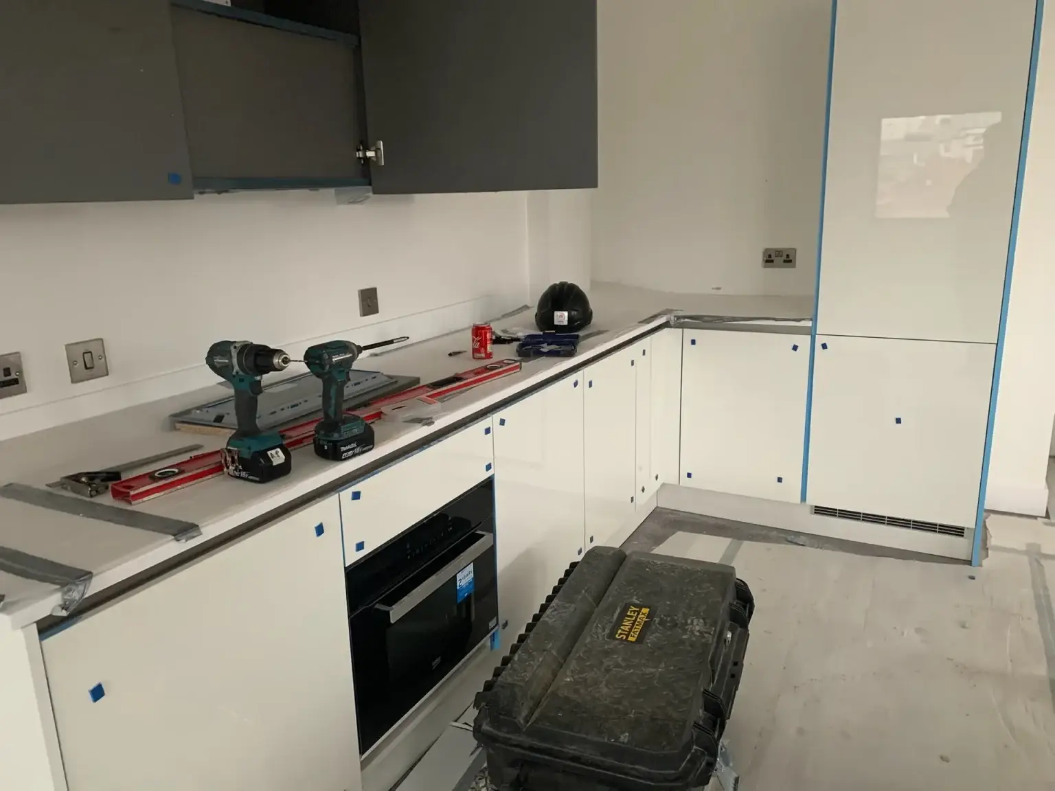 White kitchen units being fitted, with the oven in and tools on the worktop