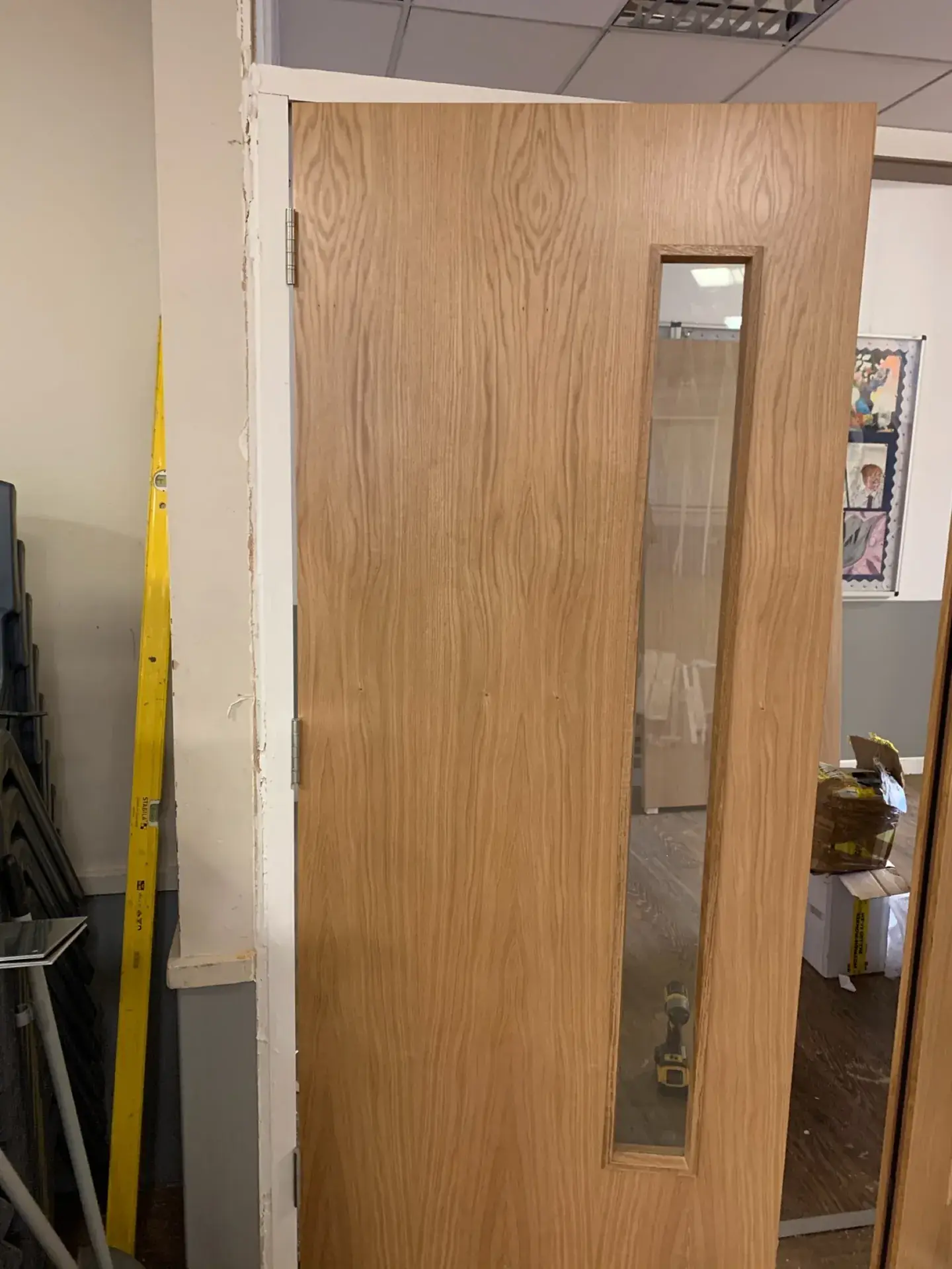 An oak-veneer door with a vision panel being hung