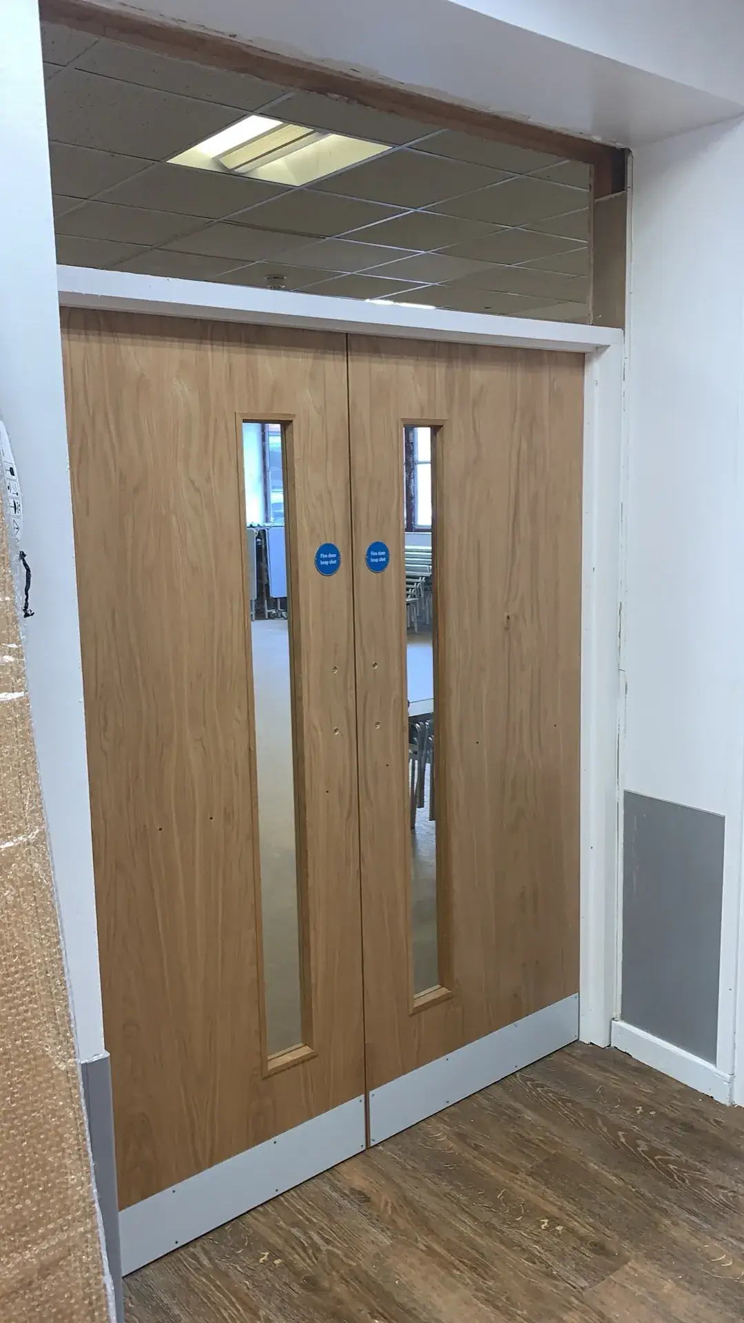 Oak-veneer double doors with vision panels in a commercial corridor