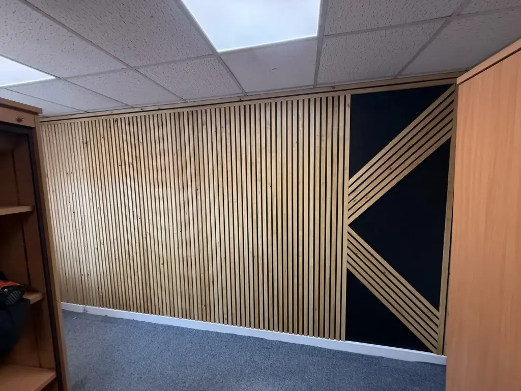 A slatted timber feature wall with a black geometric panel, in an office